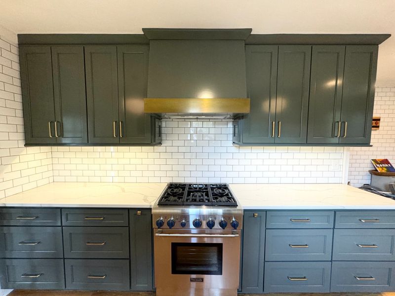 Modern kitchen with dark green cabinets, white subway tile backsplash, and stainless steel range.