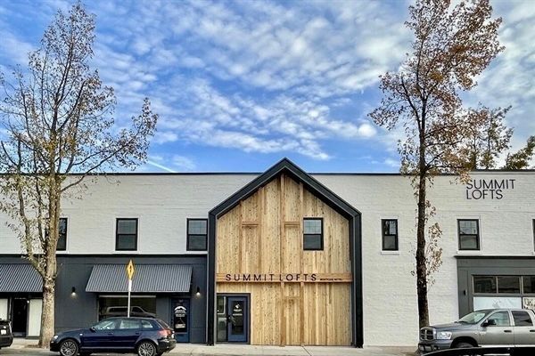 Street view of modern storefronts with a wood-front building and parked cars under a cloudy sky.