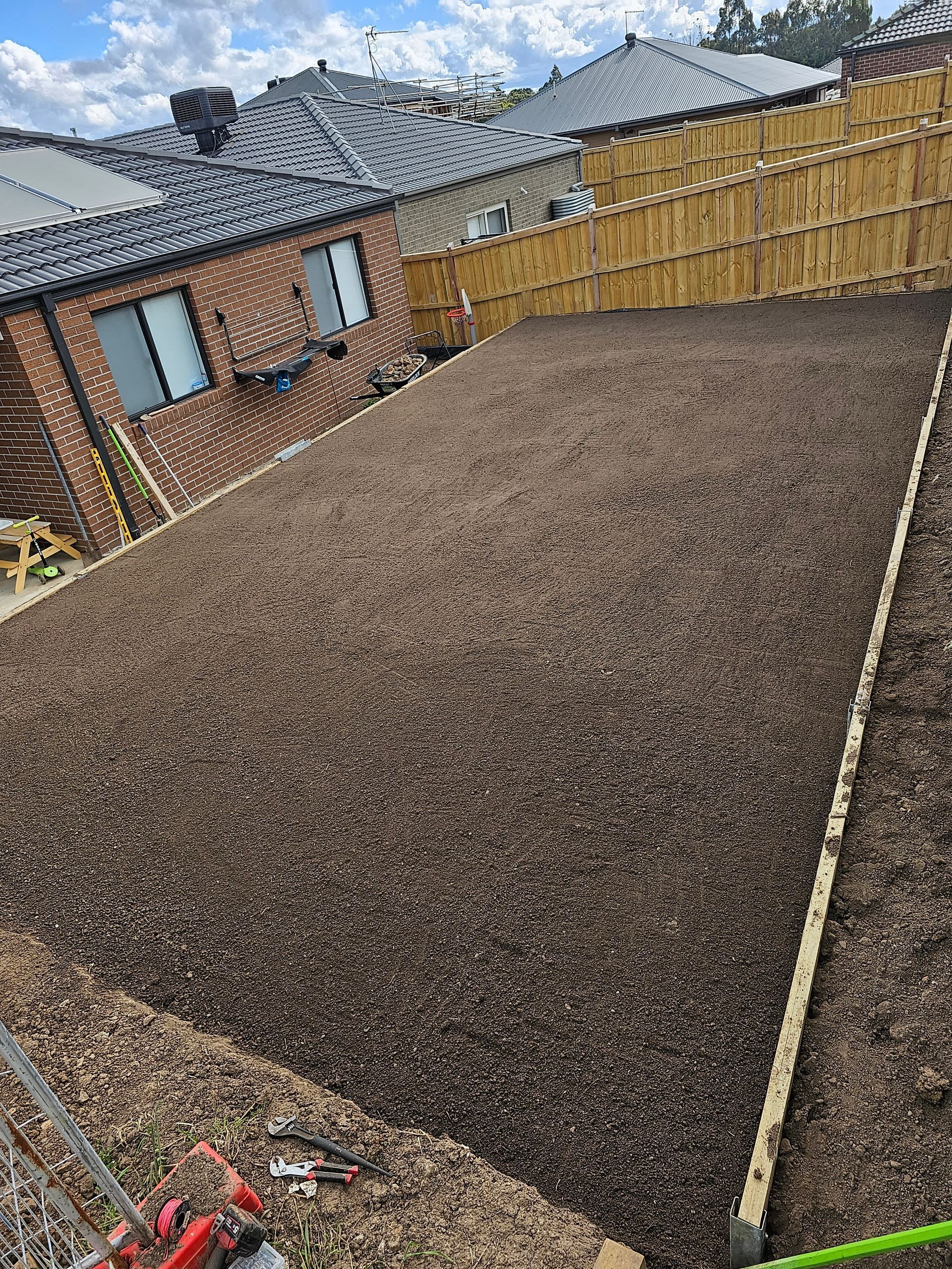 A backyard covered in dark brown mulch, with a fence and houses in the background.