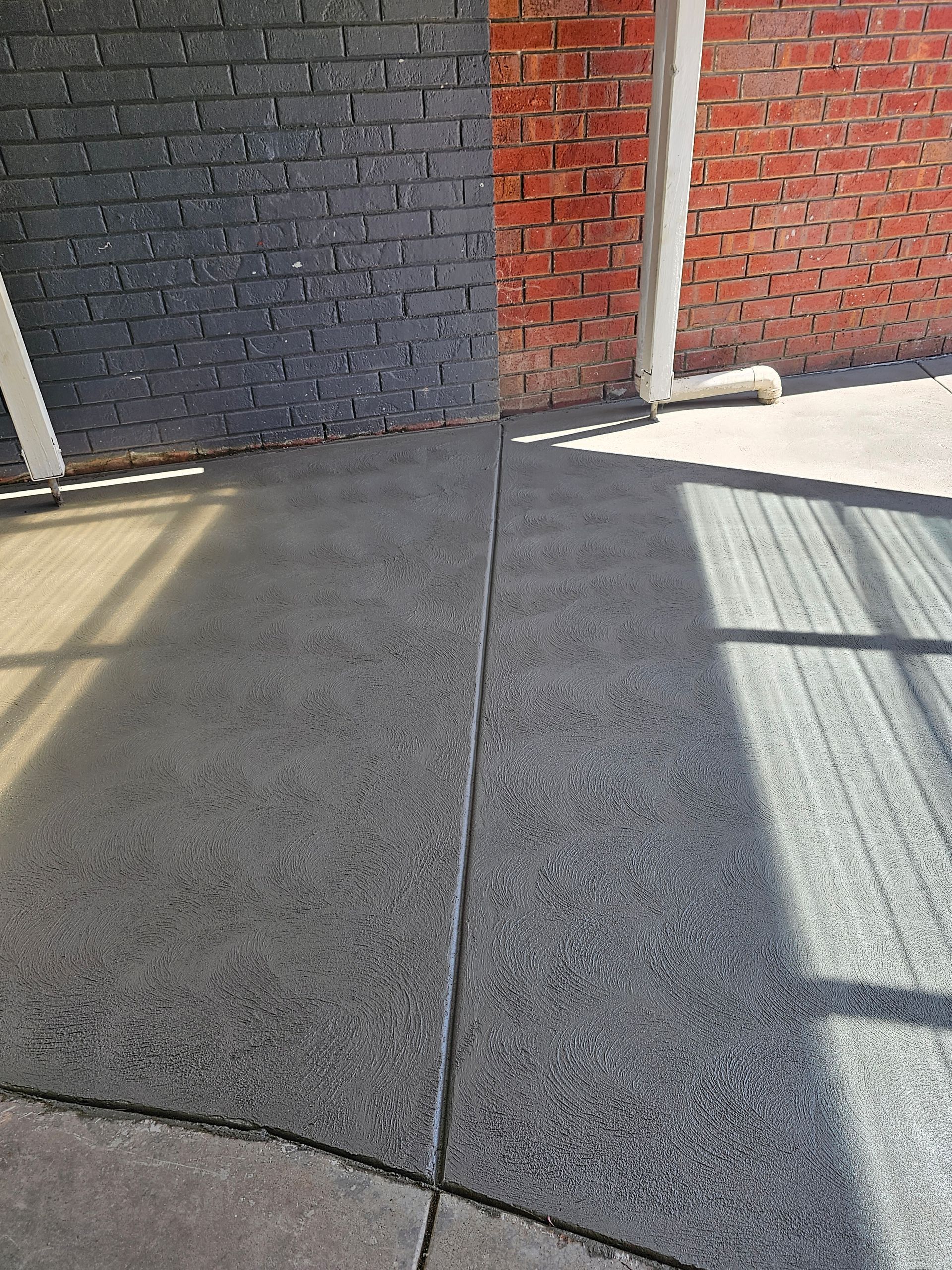 Concrete flooring, divided by a seam, next to brick walls; one painted black, the other red.