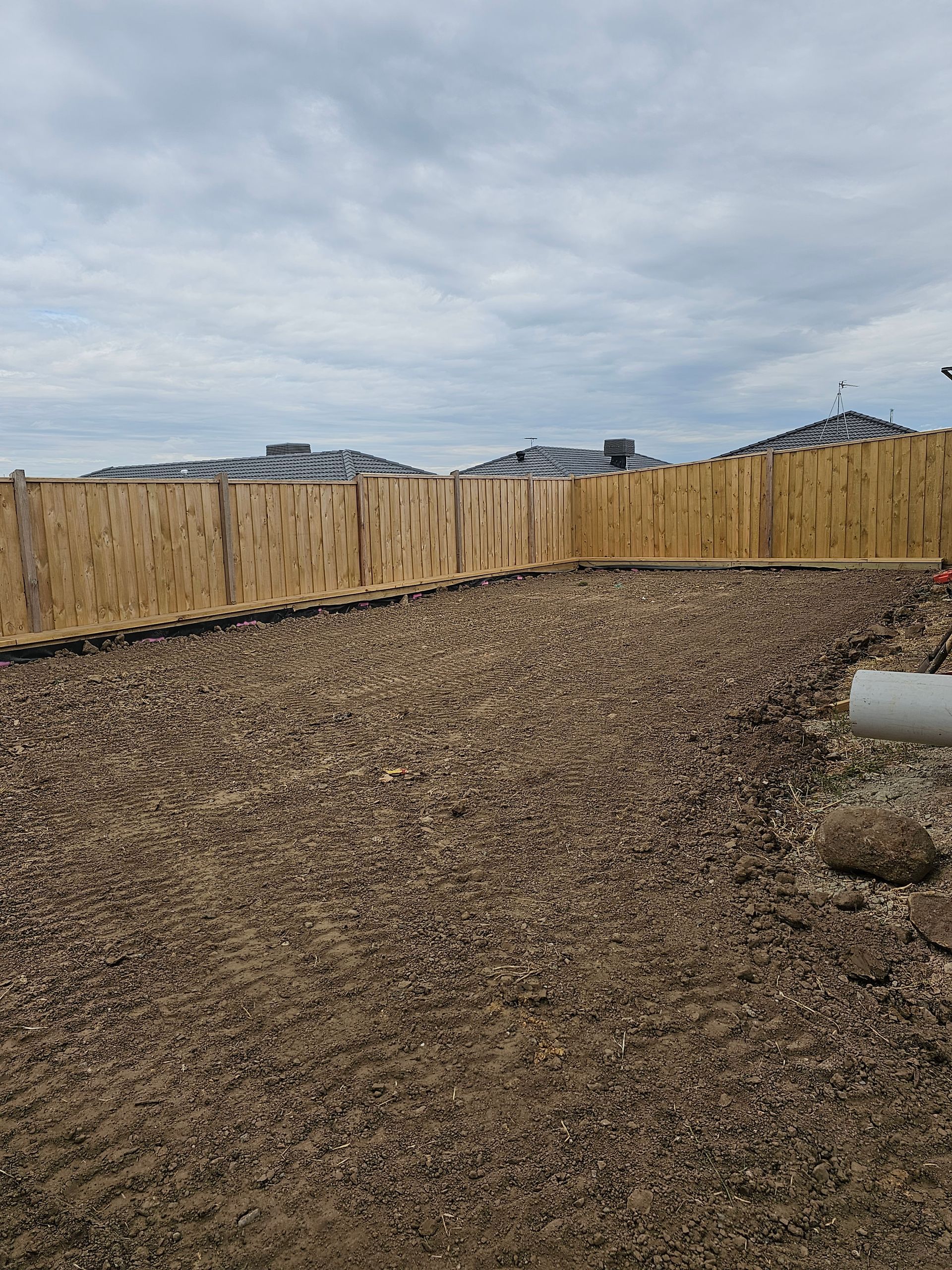 Gravel-covered backyard with a wooden fence, set against a cloudy sky and rooftops in the distance.