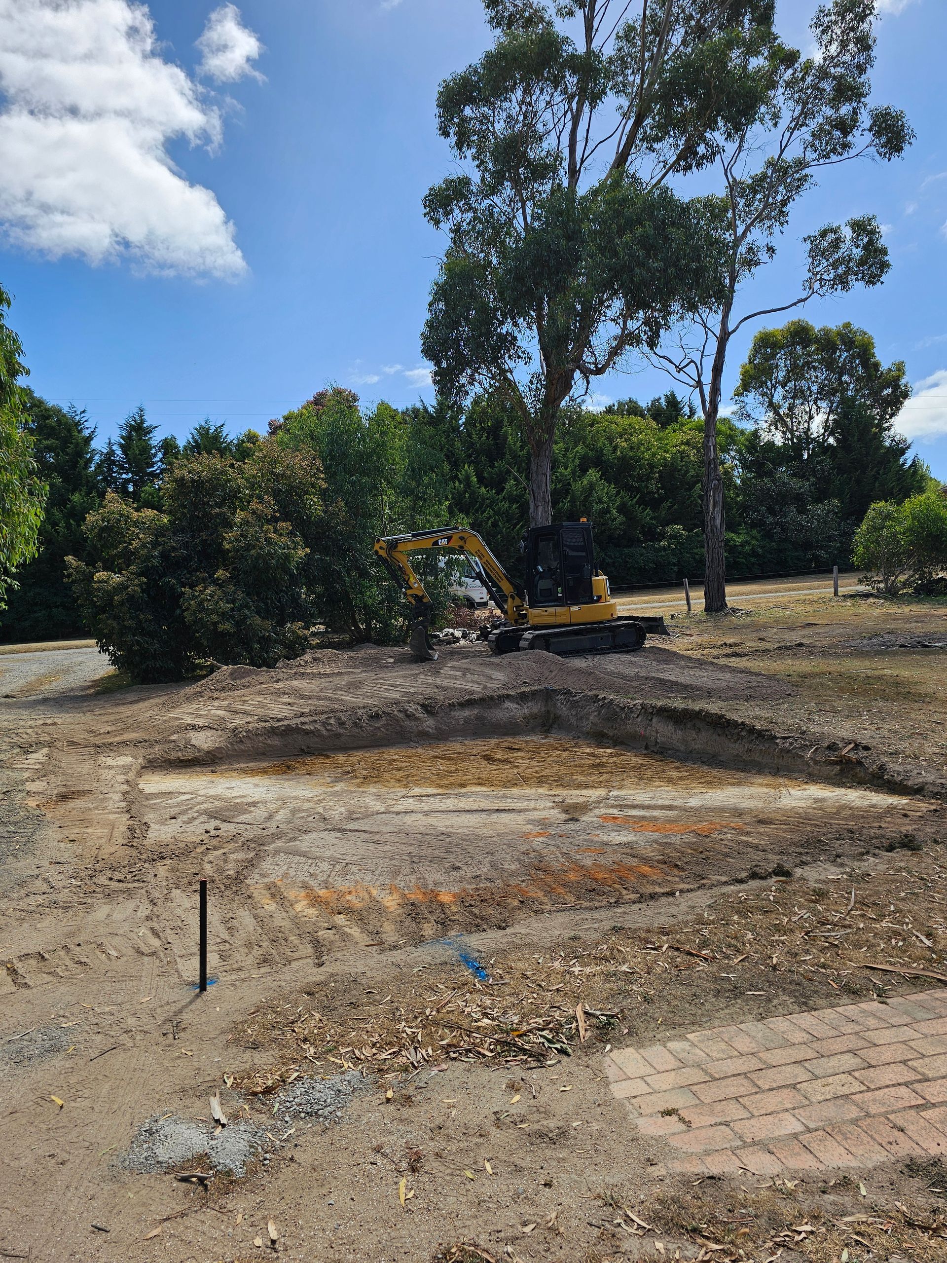 Yellow excavator clearing a tree and brush on a construction site under a blue sky. Brown and gray dirt surrounds the area.