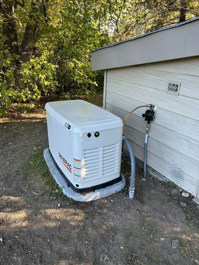 A white home generator next to a house. A grounding wire connects to the exterior wall.