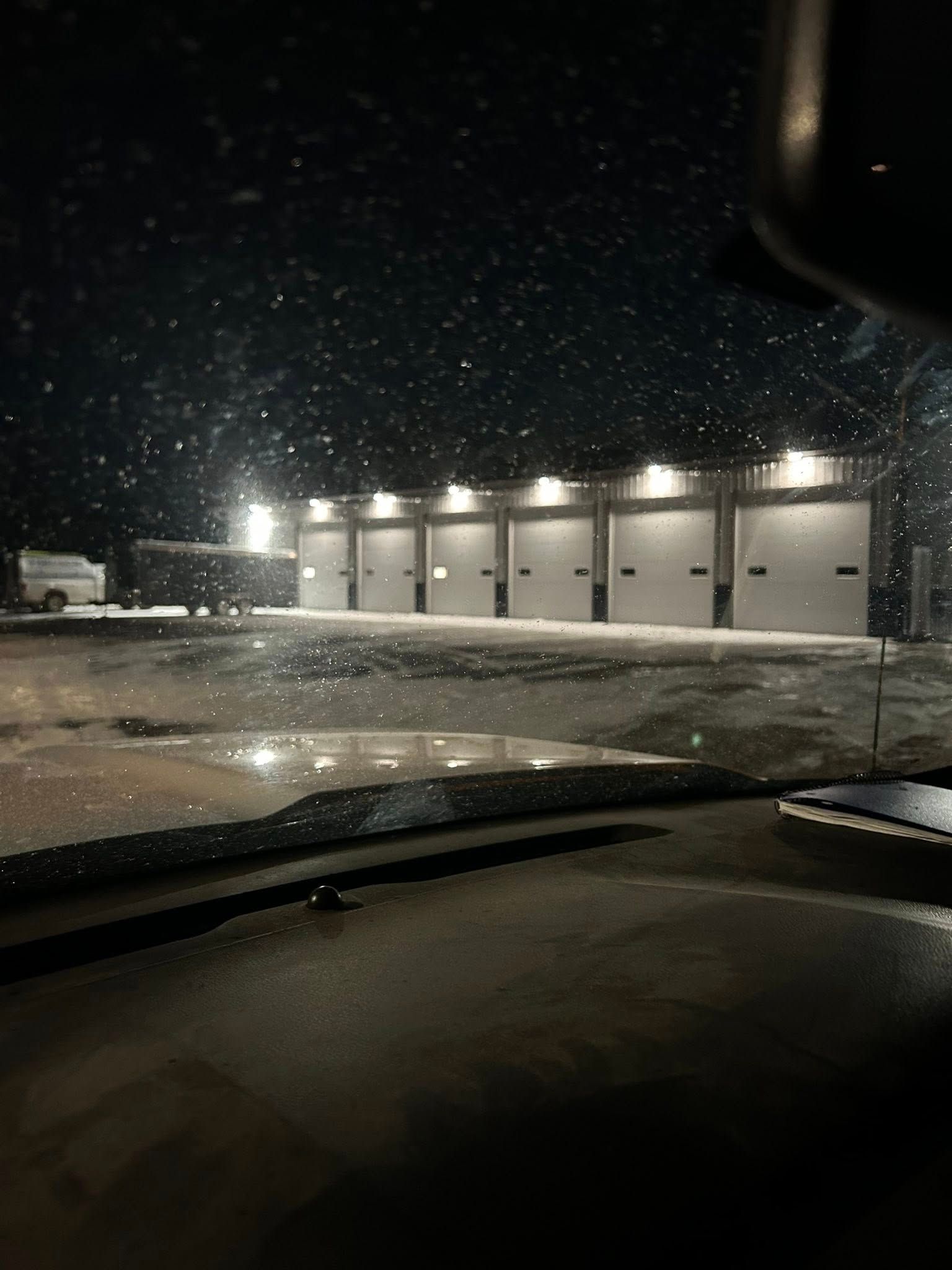 Snowy night scene: row of lit garage doors; wet pavement reflects lights.