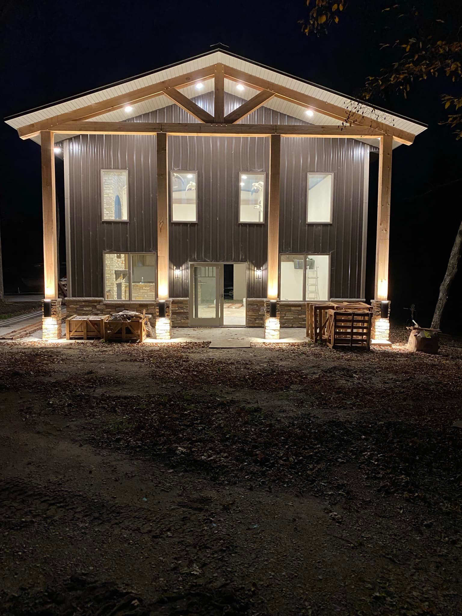 Modern two-story building at night with lights highlighting wood beams and metal siding.