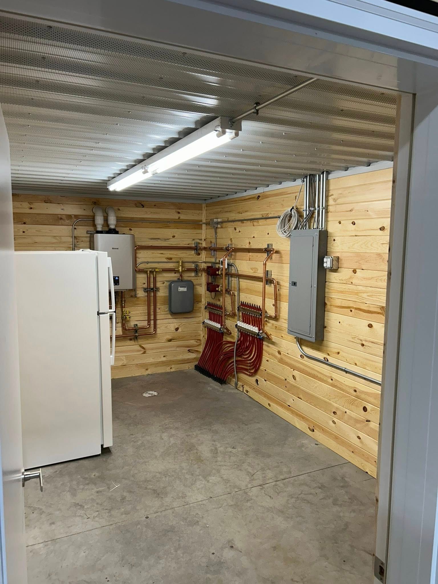 Utility room with a water heater, pipes, electrical panel, and a refrigerator.