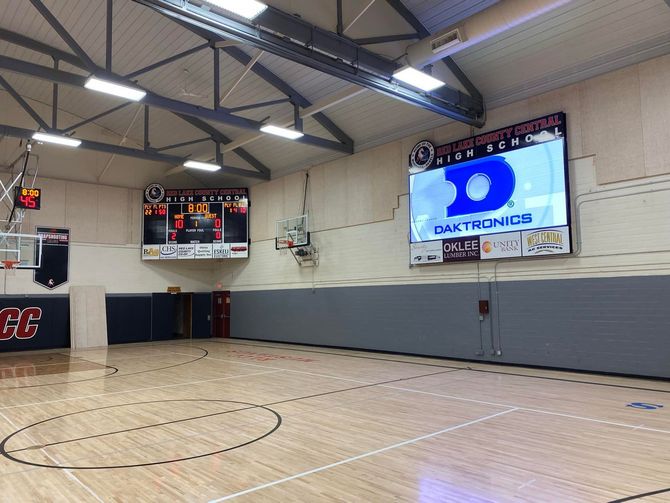 Basketball court with scoreboards, hoop, and a large screen displaying a logo.