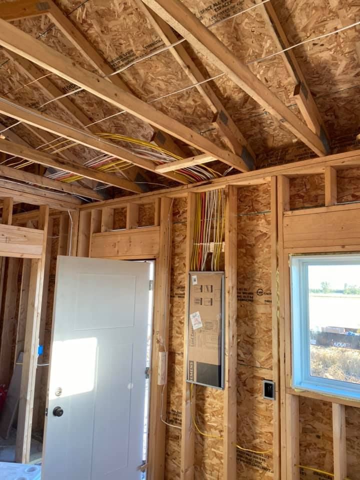 Interior of a building under construction, showing wooden framing, electrical wiring, and a door.