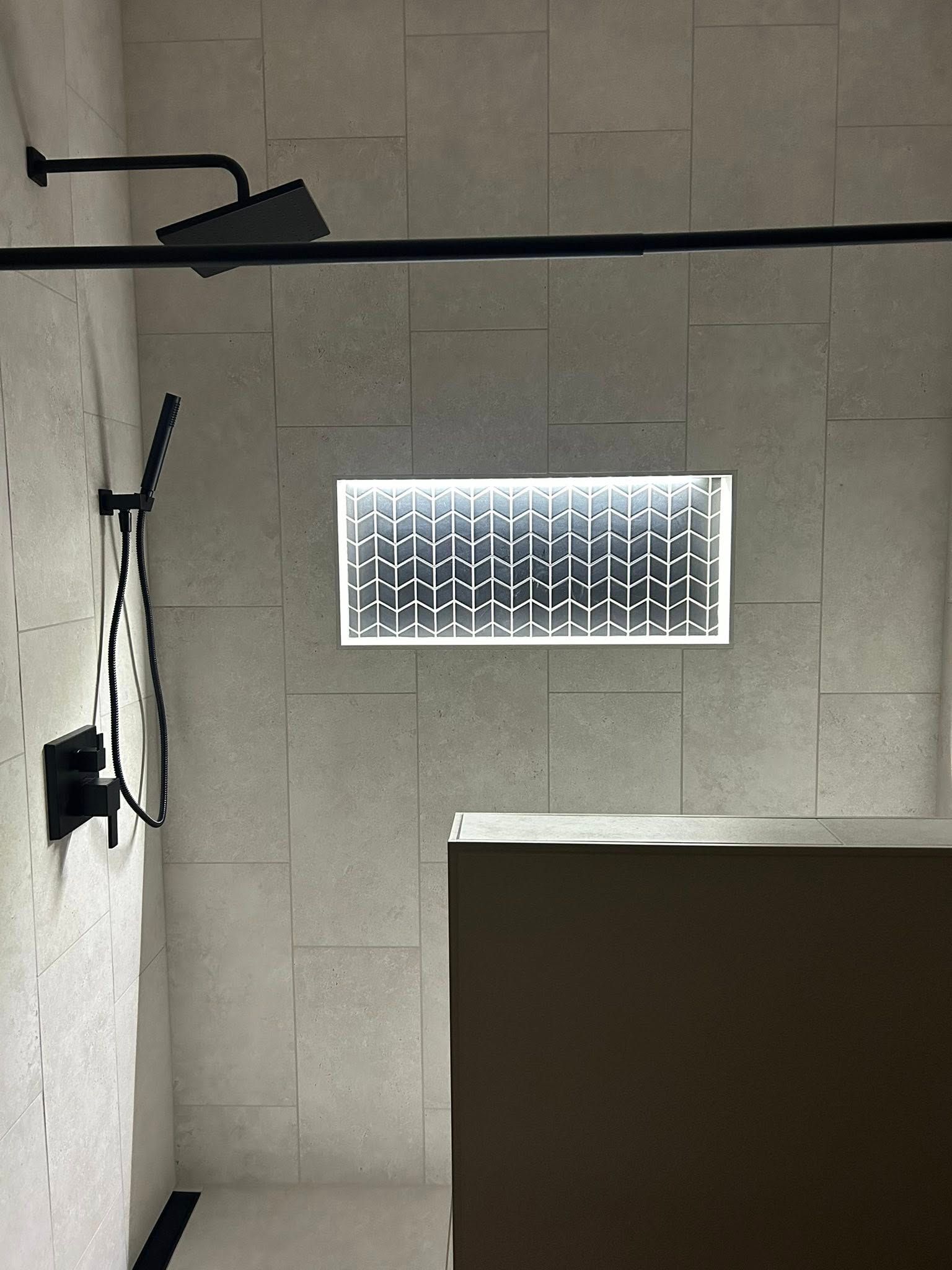 Modern shower interior with black fixtures, tile walls, and a lit, recessed niche.