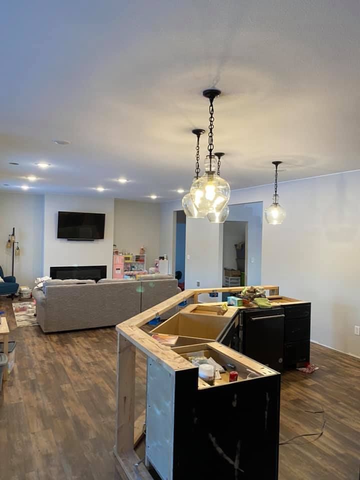 Kitchen under renovation with island, light fixtures, living area with couch and fireplace.