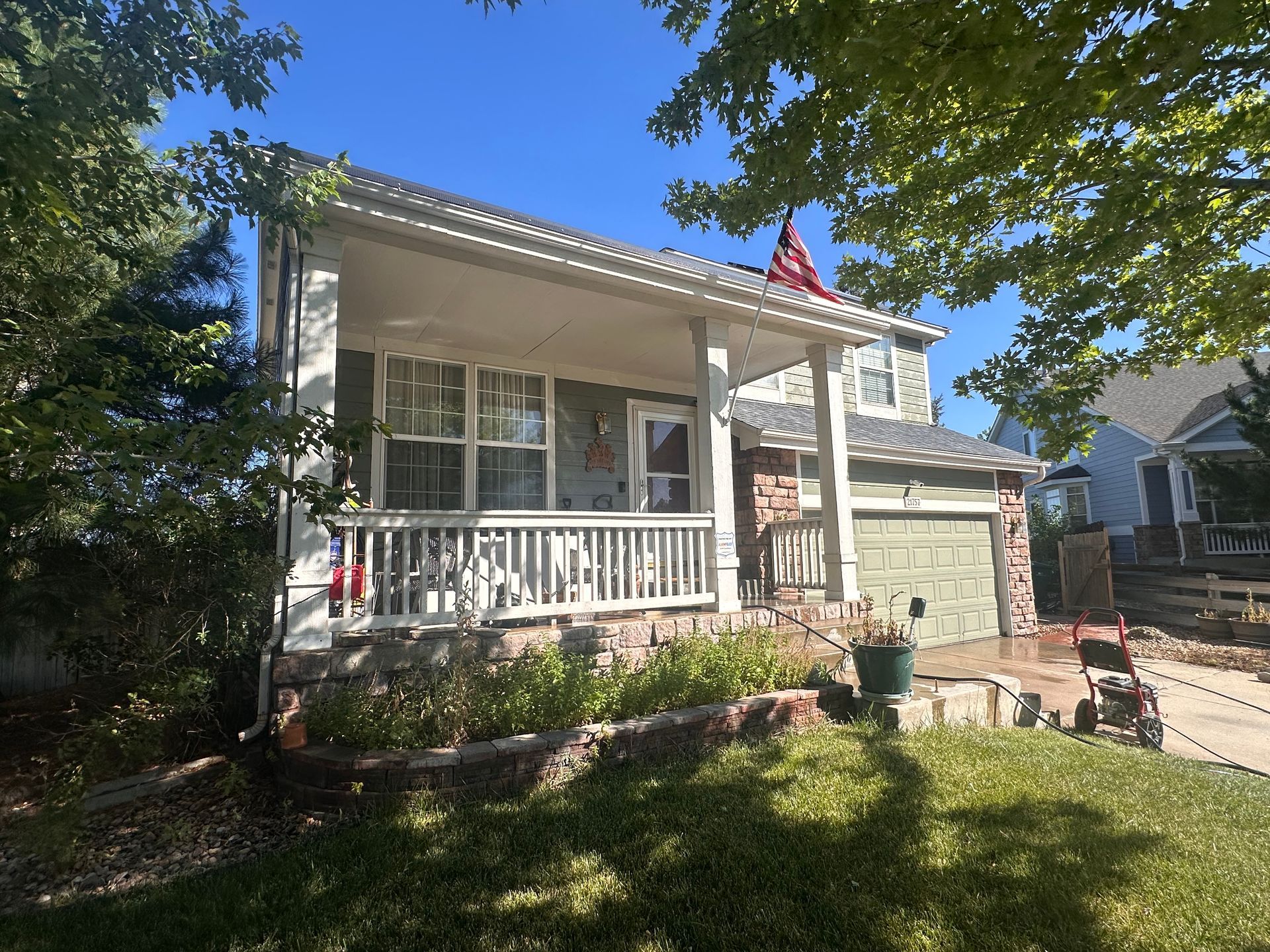 A two-story house with a front porch, green siding, stone accents, and a US flag.