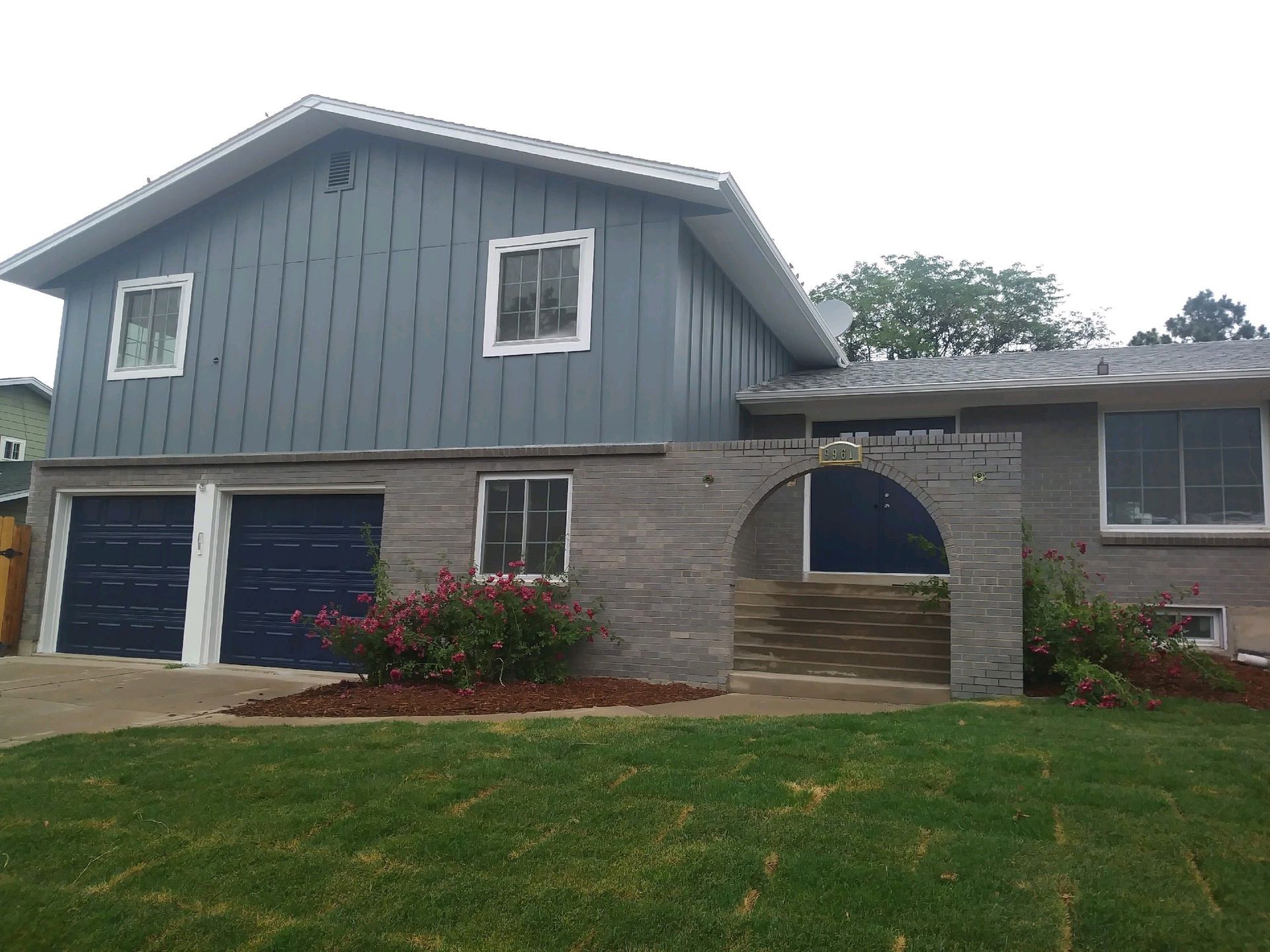 Two-story house with blue siding and garage doors, stone facade, arch doorway, and green lawn.