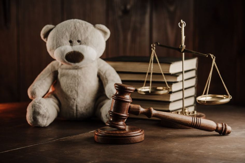 A teddy bear is sitting next to a judge 's gavel and scales of justice.