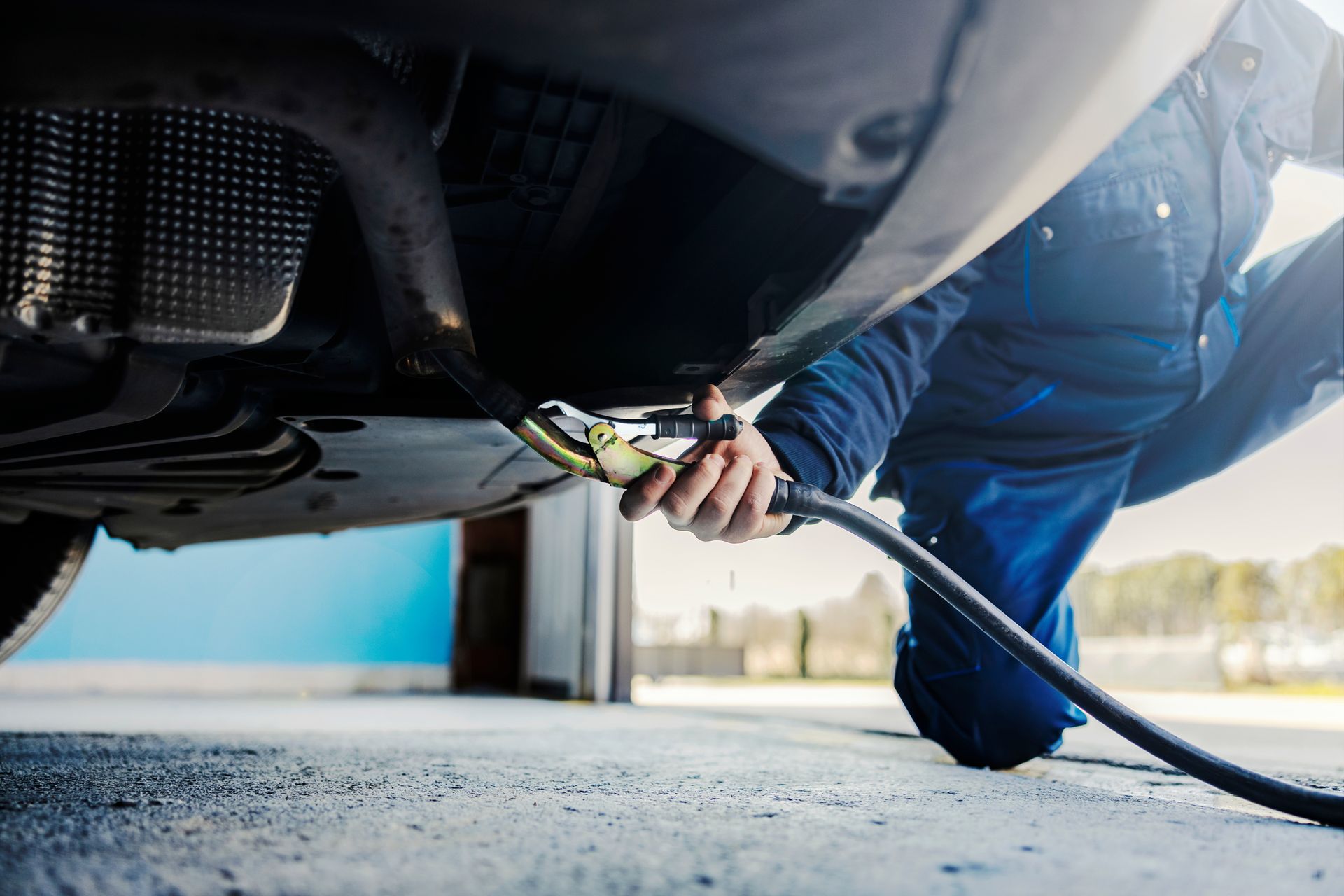Mechanic in blue uniform fueling a car from underneath with a hose and nozzle Mechanic in blue uniform fueling a car from underneath with a hose and nozzle