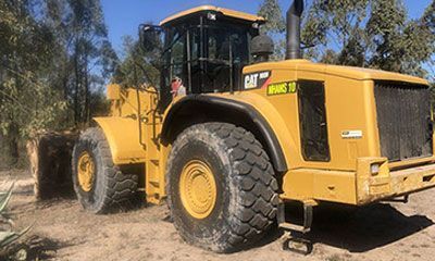 A large yellow tractor is parked in the dirt.
