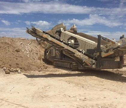 A large machine is sitting in the middle of a dirt field.