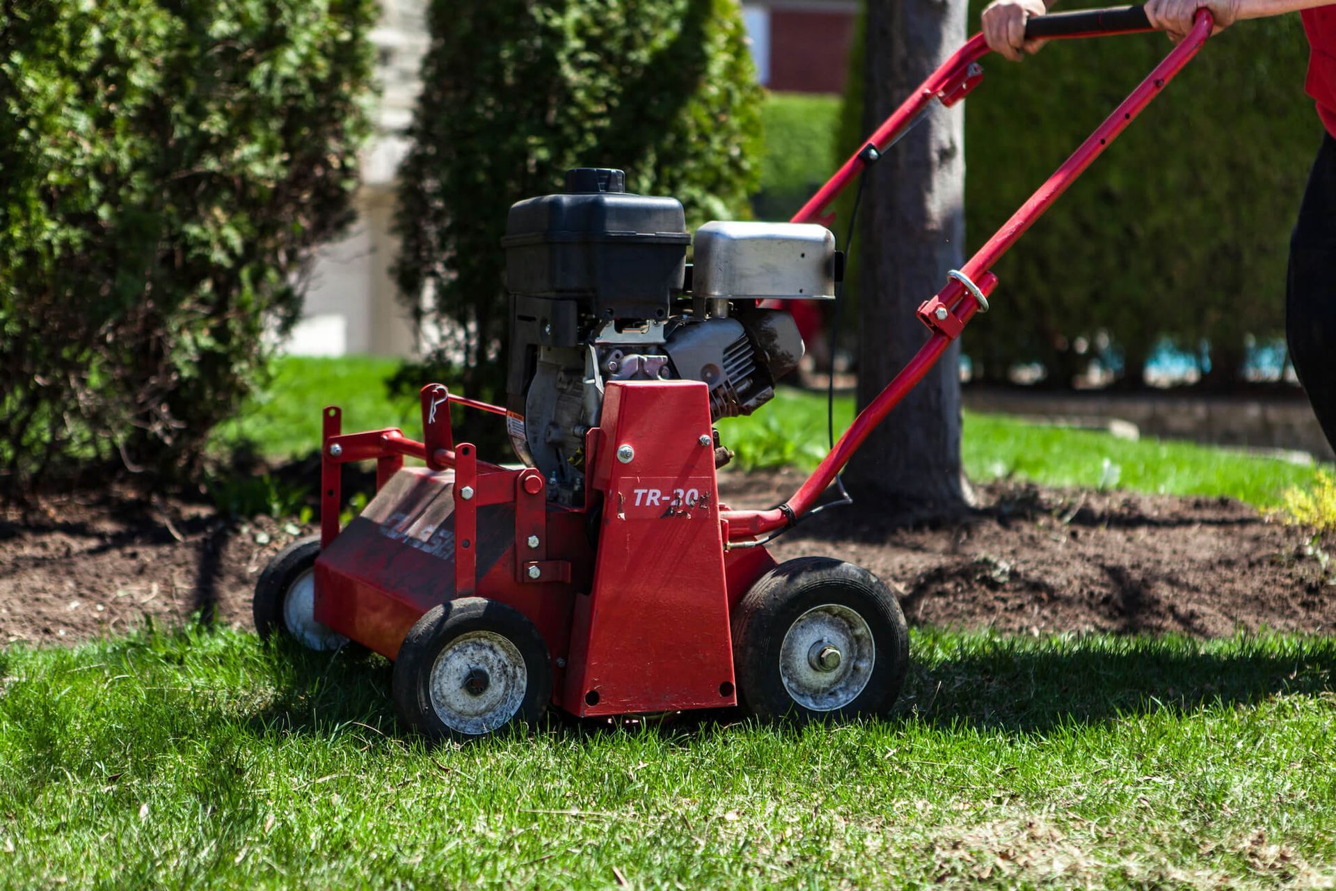 Red lawn aerator on grass beside a red extension arm in a landscaped yard