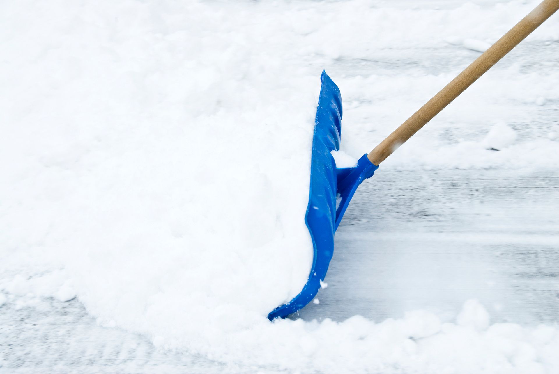 Blue snow shovel pushing a mound of snow on a white, snowy surface