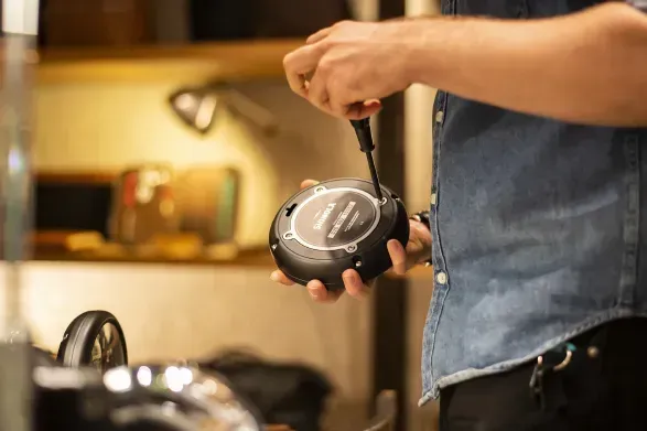 Person using a screwdriver to assemble a small, round, black device with a label.