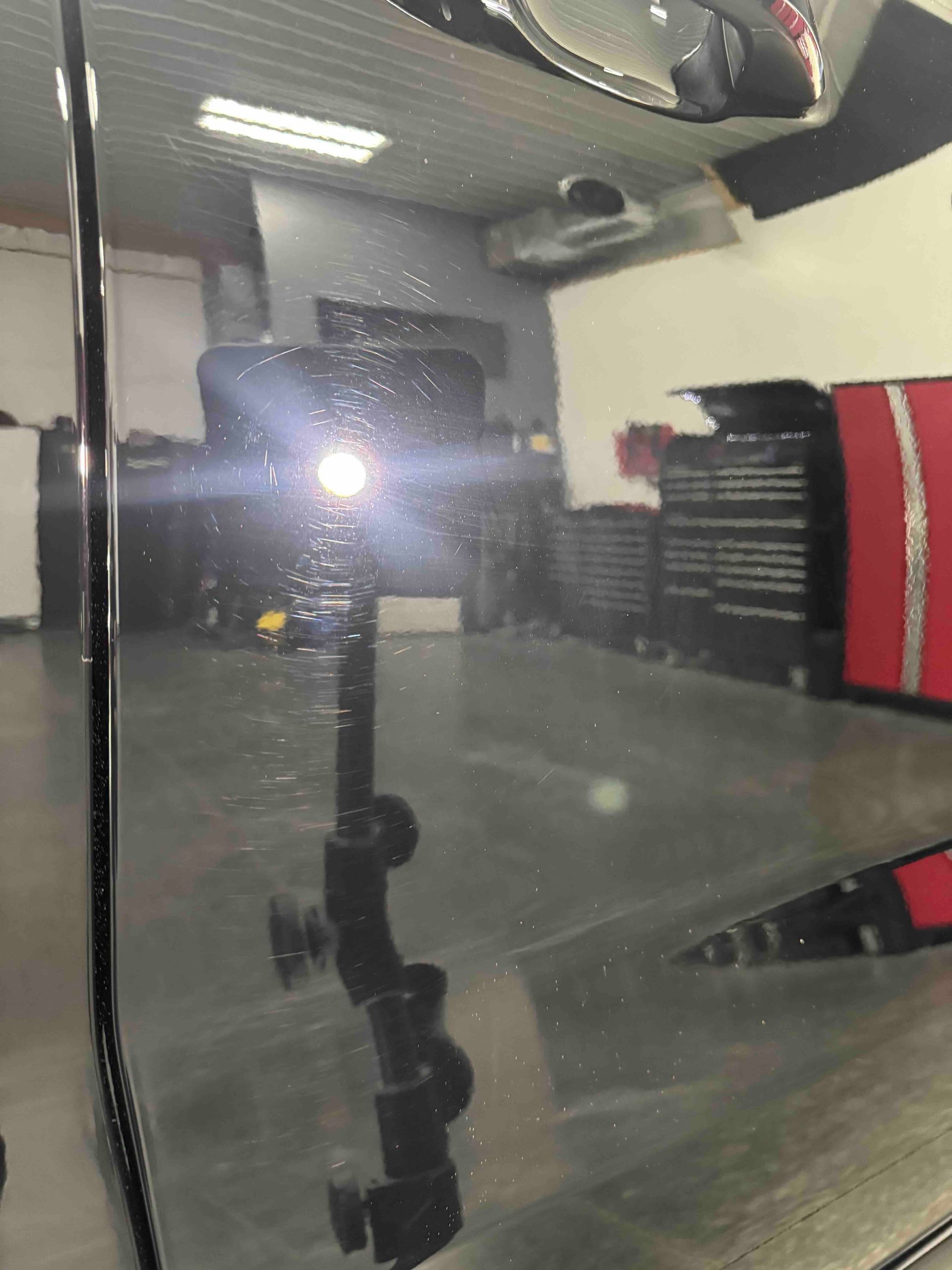 Black car panel reflecting a bright light in a garage setting with tools.