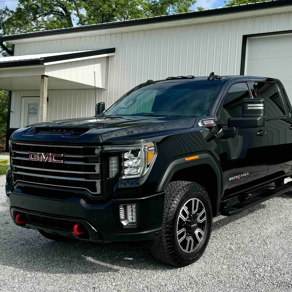 Black GMC truck parked in front of a white building with open garage door.