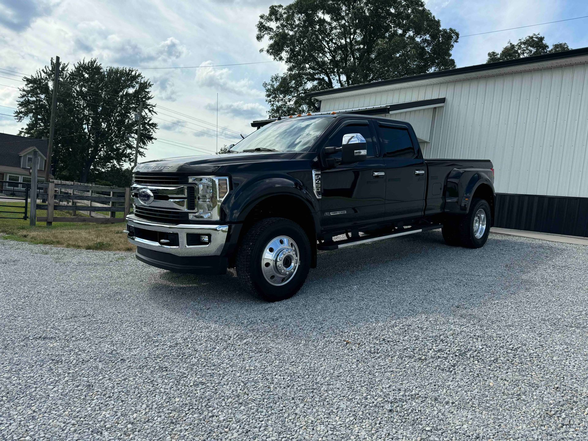 Black Ford pickup truck parked on gravel next to a white building under a cloudy sky.