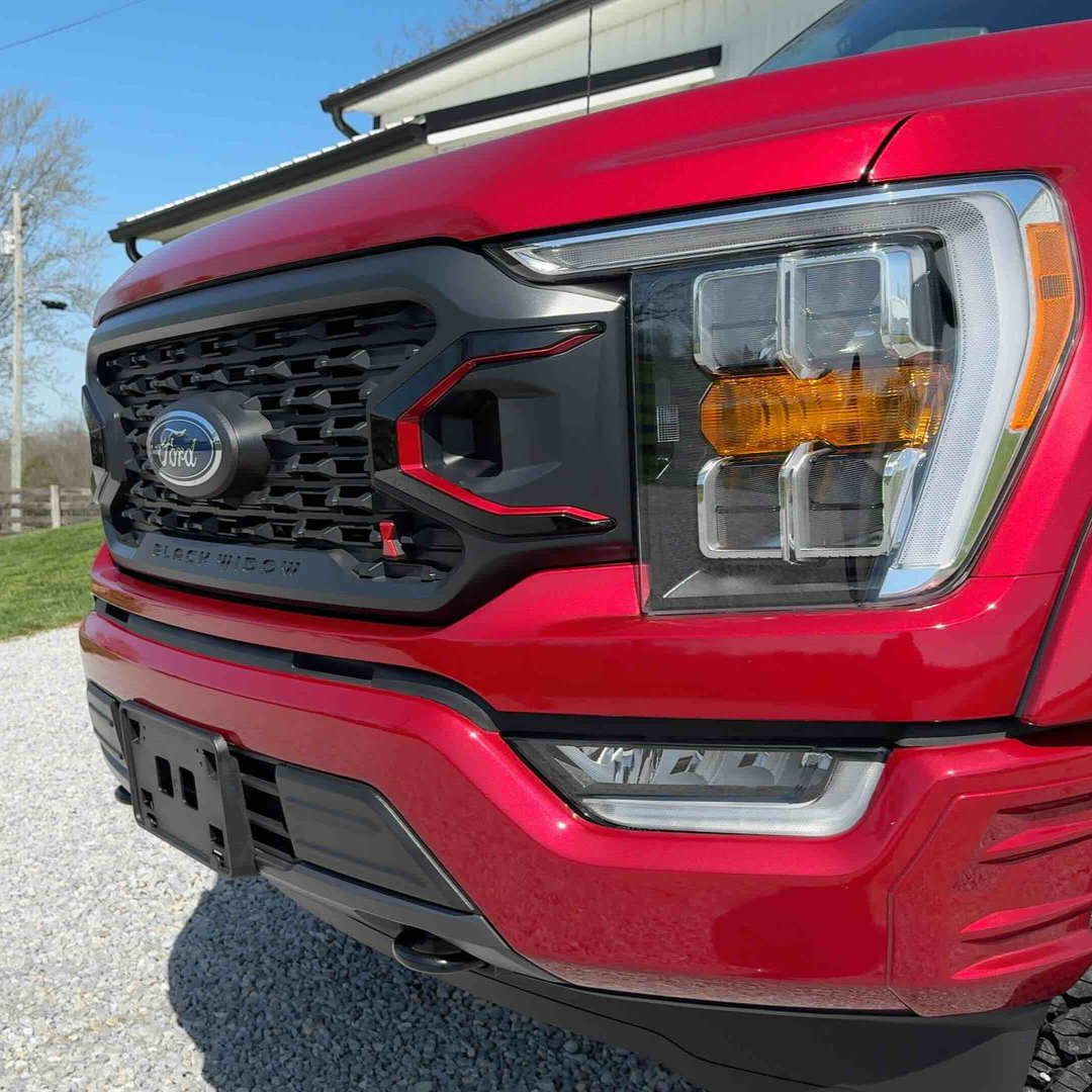 Red Ford F-150 truck front with black grille and headlight detail, parked outside on a sunny day.
