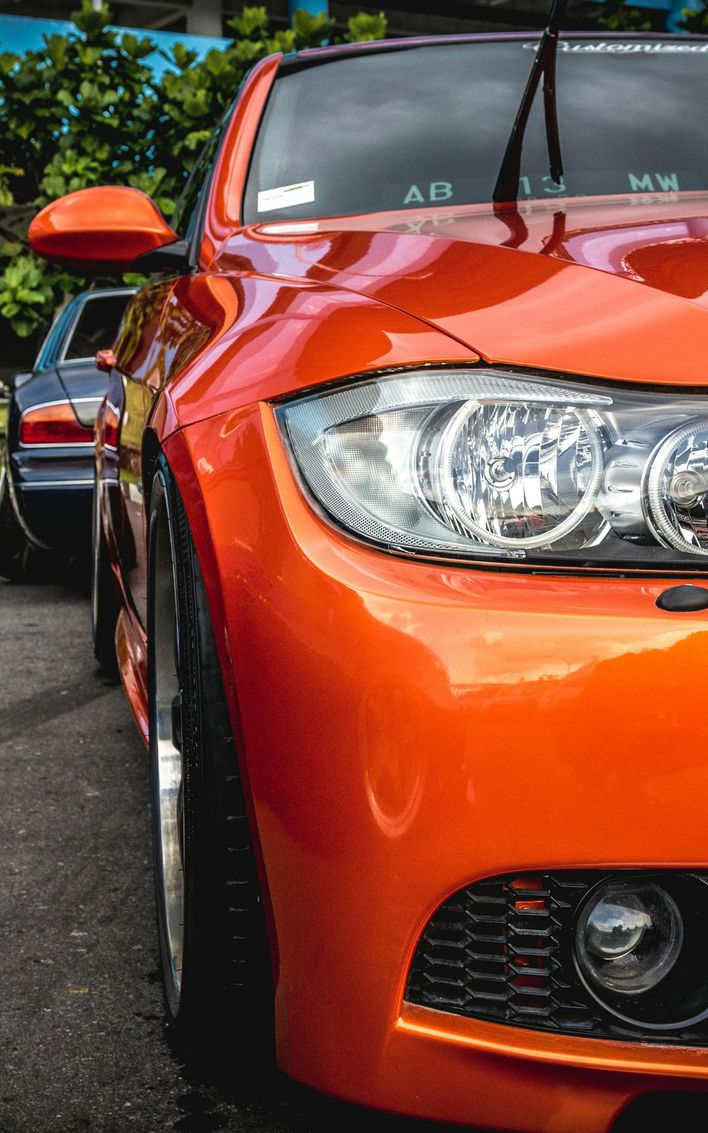 Orange BMW car's front side with a shiny, reflective surface; parked near another car.