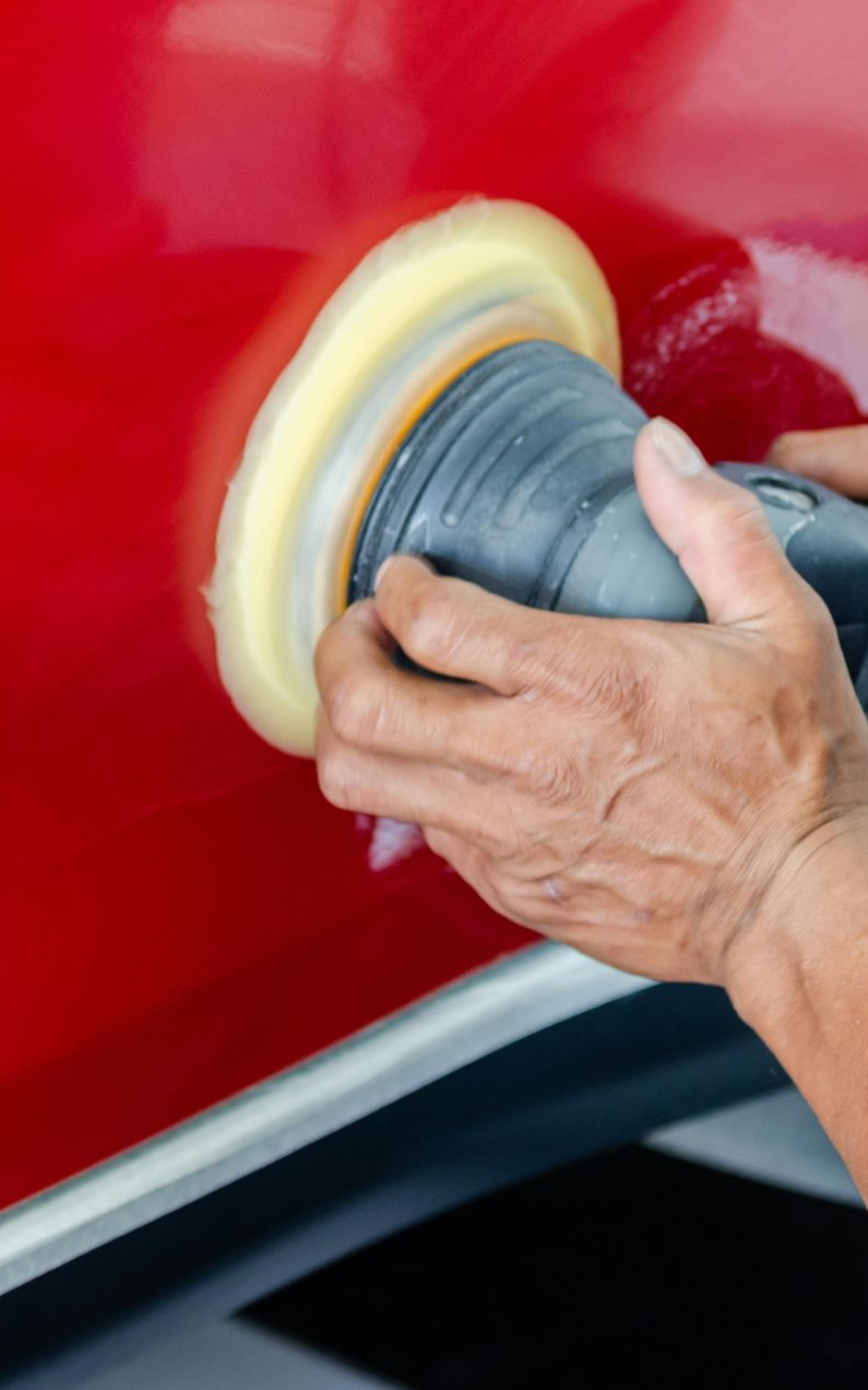 Person using a buffer on a red car, applying polish to the paint.