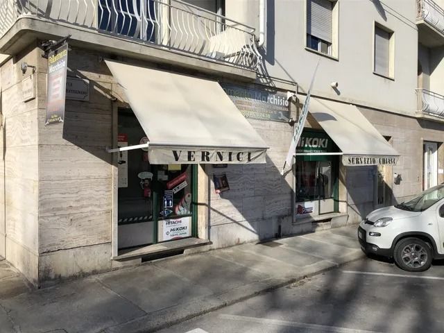 Vetrina di un negozio con tende da sole beige su una strada soleggiata, con un'auto bianca parcheggiata sul marciapiede.