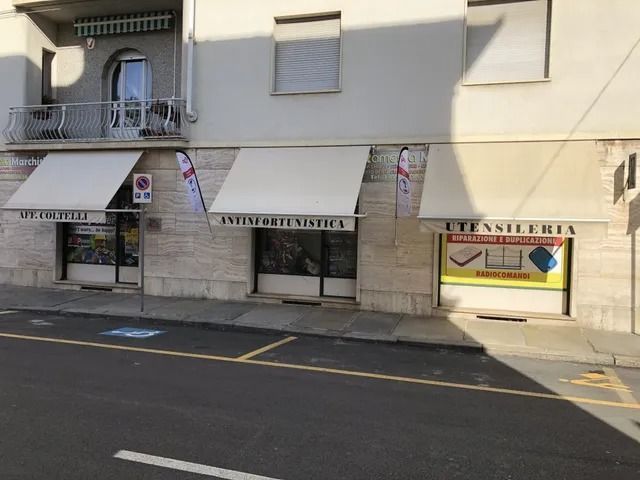 Vetrine su una strada soleggiata con balconi e tende da sole a righe, tra cui l'insegna di una lavanderia a gettoni.