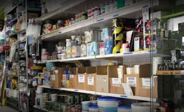 Scaffali pieni di vernici e articoli di ferramenta assortiti in un corridoio disordinato di un negozio.