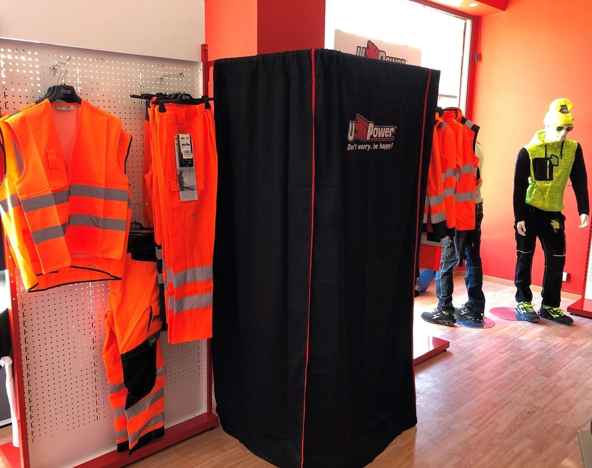 Esposizione di dispositivi di sicurezza con giubbotti riflettenti arancioni e cabina spogliatoio nera in un negozio