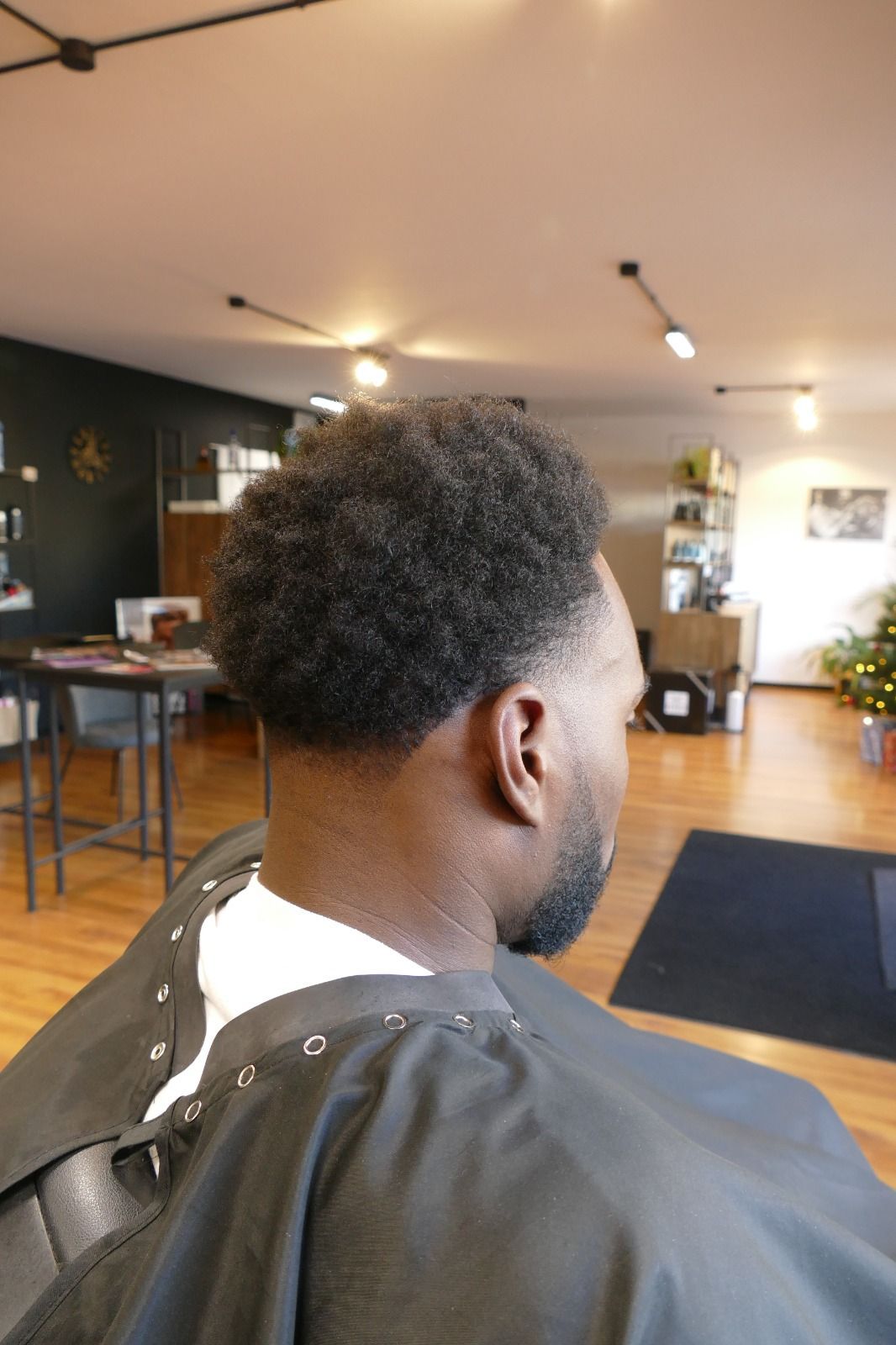 Un uomo si fa tagliare i capelli dal barbiere. Ha capelli scuri, corti e voluminosi. L'ambiente del barbiere è caldo e accogliente.