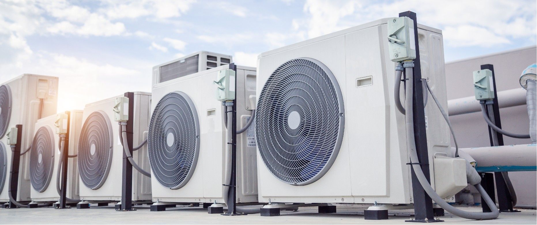 Row of outdoor air conditioning units with large fan grilles along a building wall