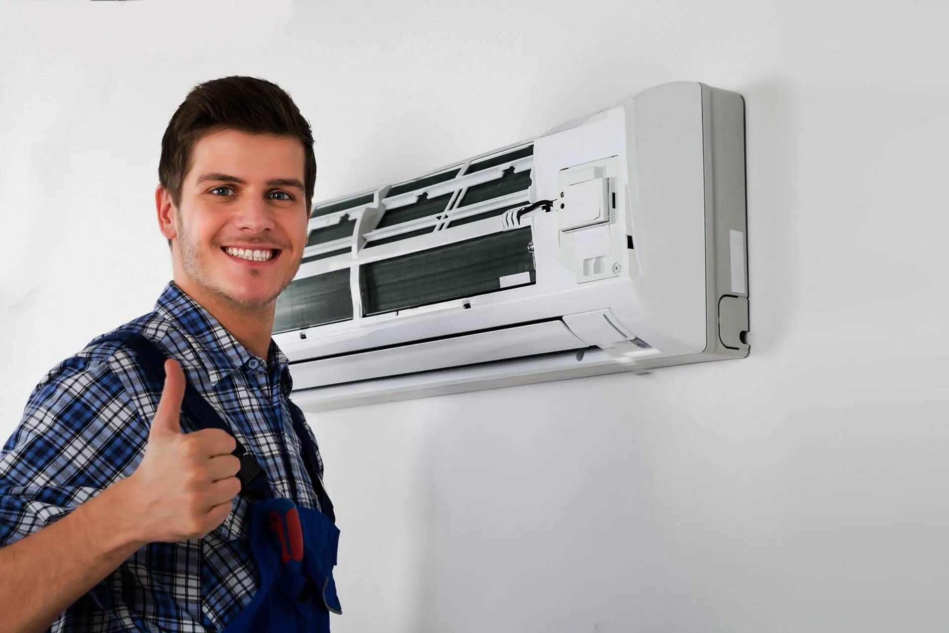Smiling technician giving a thumbs-up beside a wall-mounted air conditioner