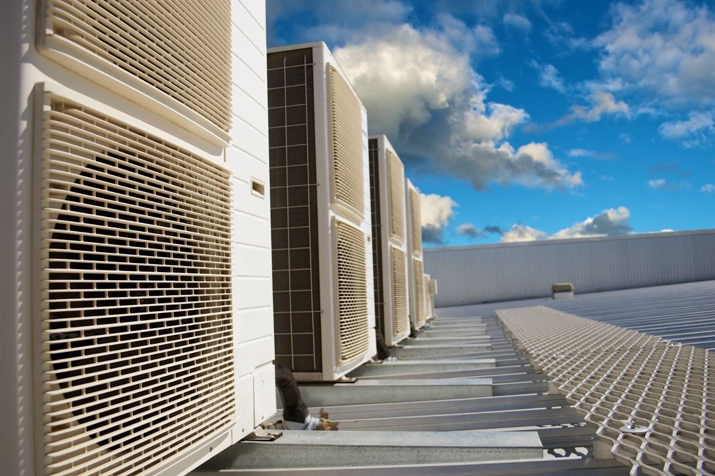 Row of beige HVAC units on a rooftop walkway under a blue sky