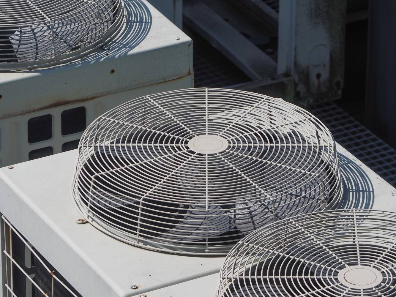 Outdoor HVAC unit with three large metal cooling fans on a rooftop.