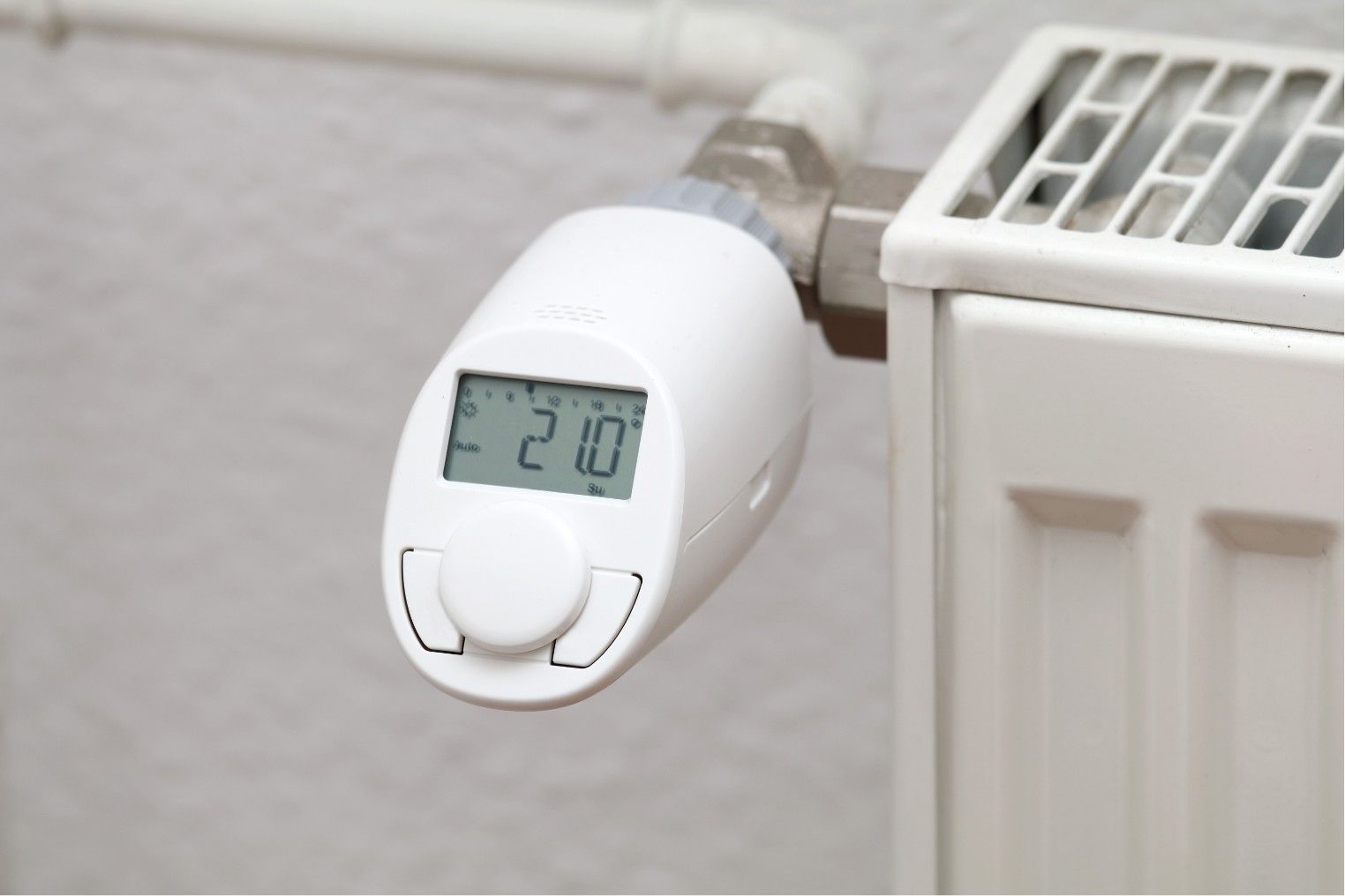 Digital radiator thermostat displaying 21°C mounted on a white heater pipe