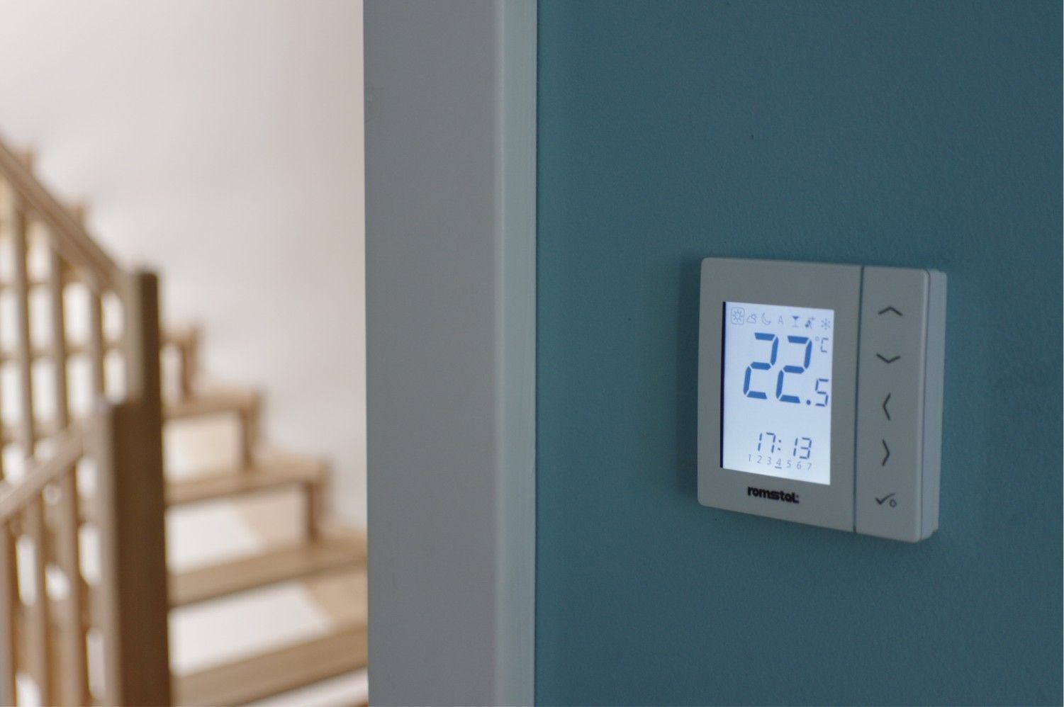 Wall thermostat on a blue wall beside a staircase, displaying 22 degrees.