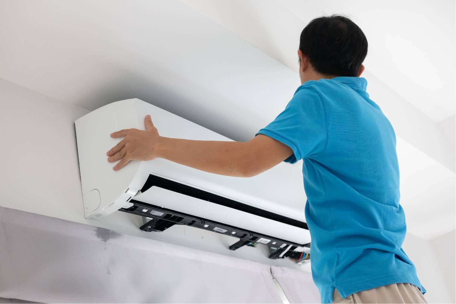 Technician installing a white wall-mounted air conditioner indoors with the front panel open