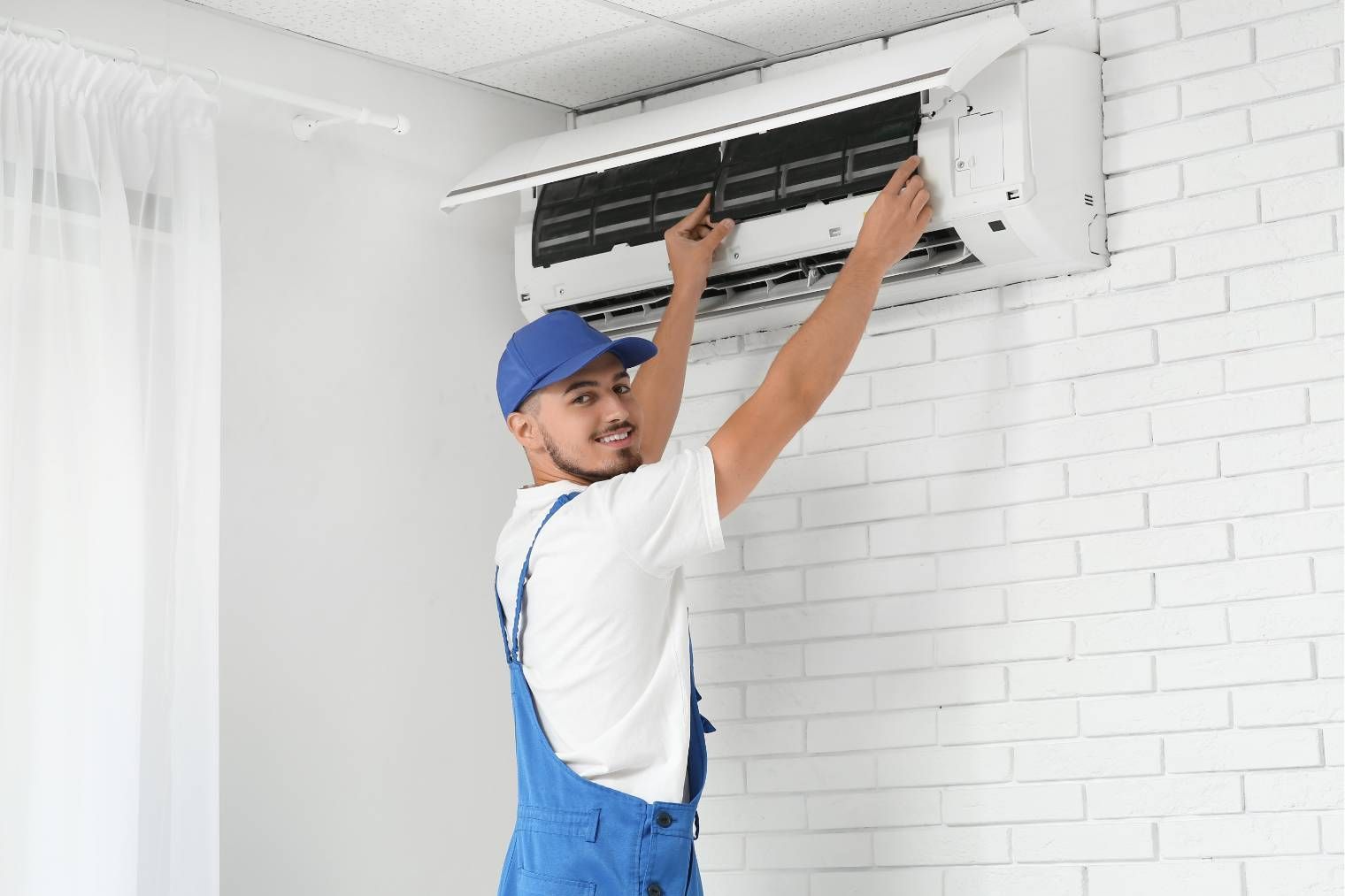 Technician repairing a wall-mounted air conditioner in a bright room