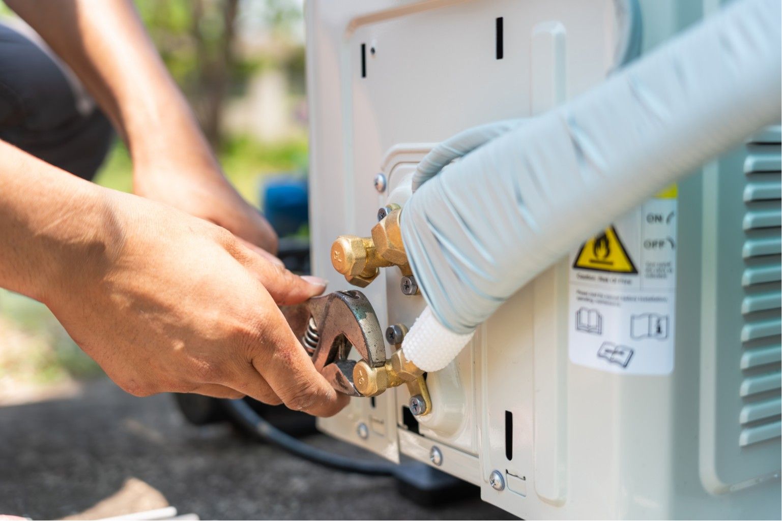 Gloved hands connecting a gas line to the back of an outdoor appliance