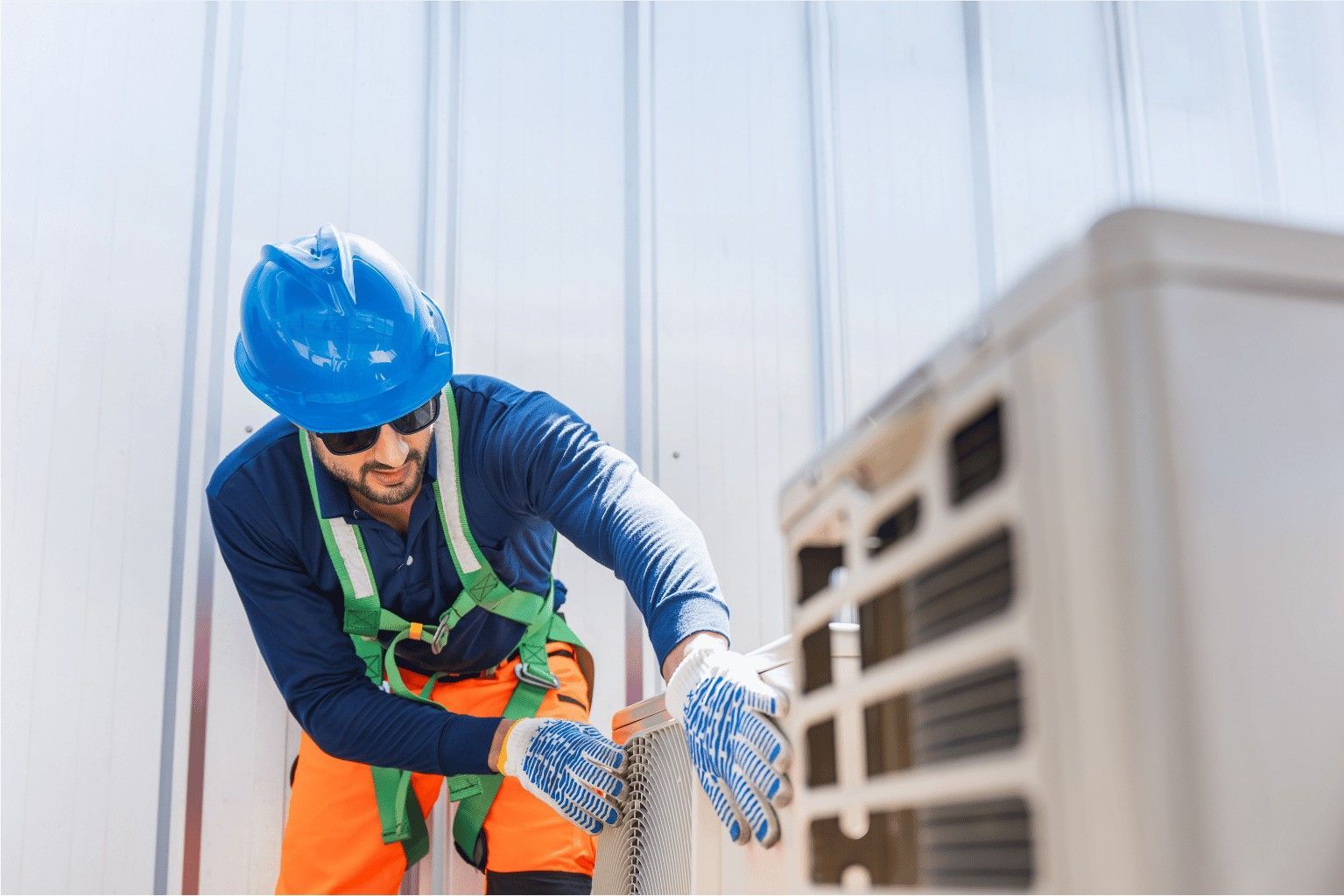 Worker in blue hard hat and safety vest inspecting equipment in an industrial setting.