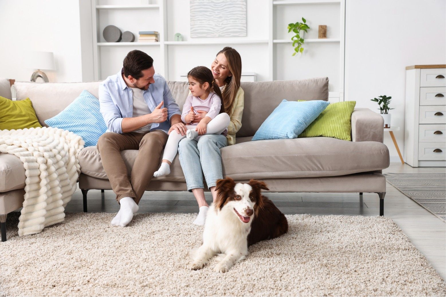 Family sitting on a sofa with a dog on a white rug in a bright living room