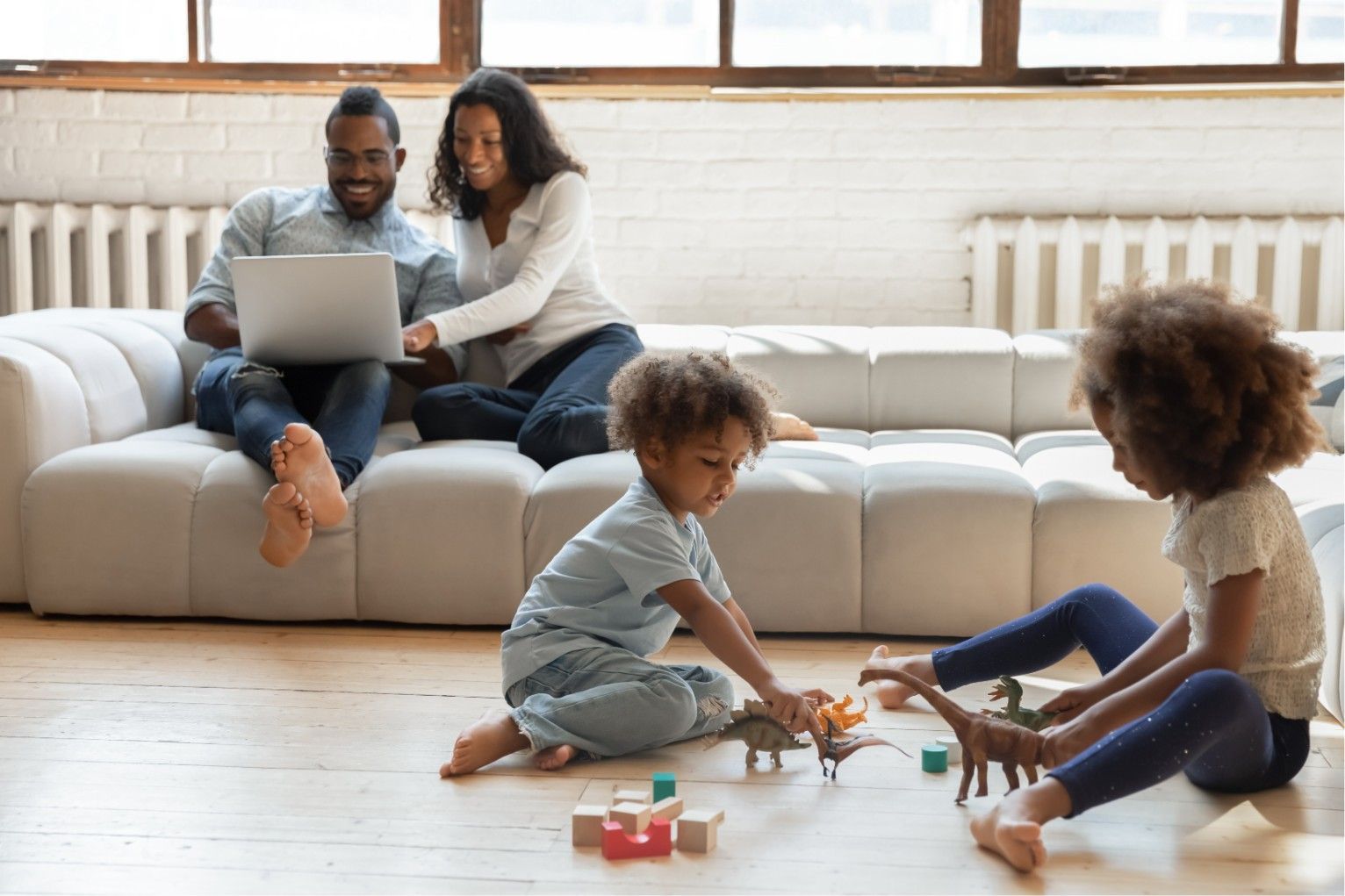 Family relaxing in a bright living room, with adults on a couch and two children playing on the floor.