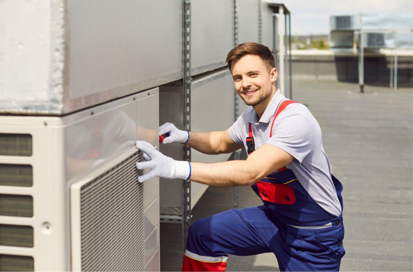 Technician in blue coveralls and red gloves servicing an outdoor HVAC unit on a rooftop
