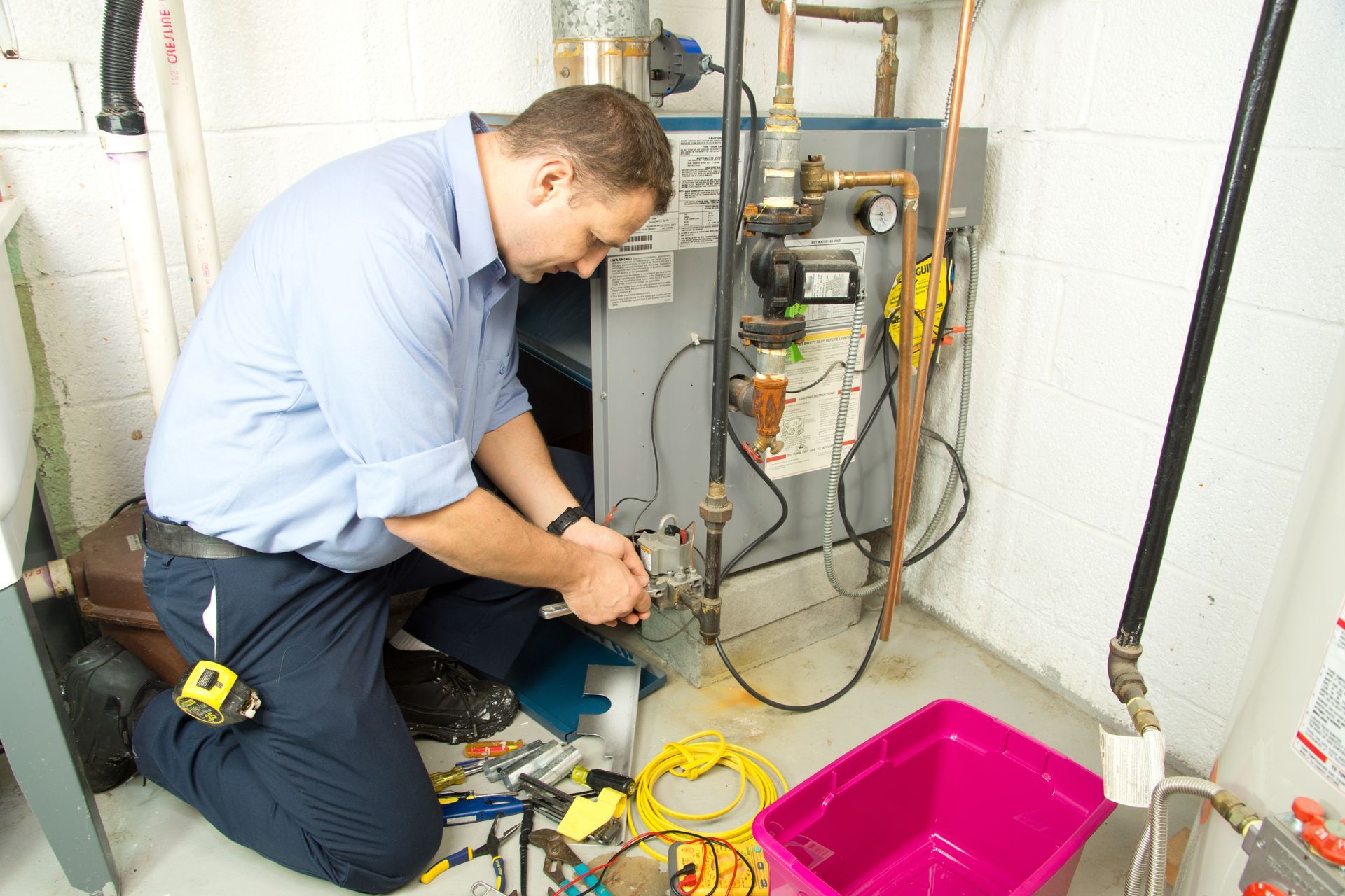Technician inspecting a large blue-gray boiler and exposed pipes in a utility room