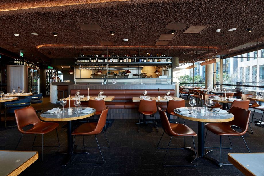 Restaurant interior with tables overlooking a bridge through large windows at sunset