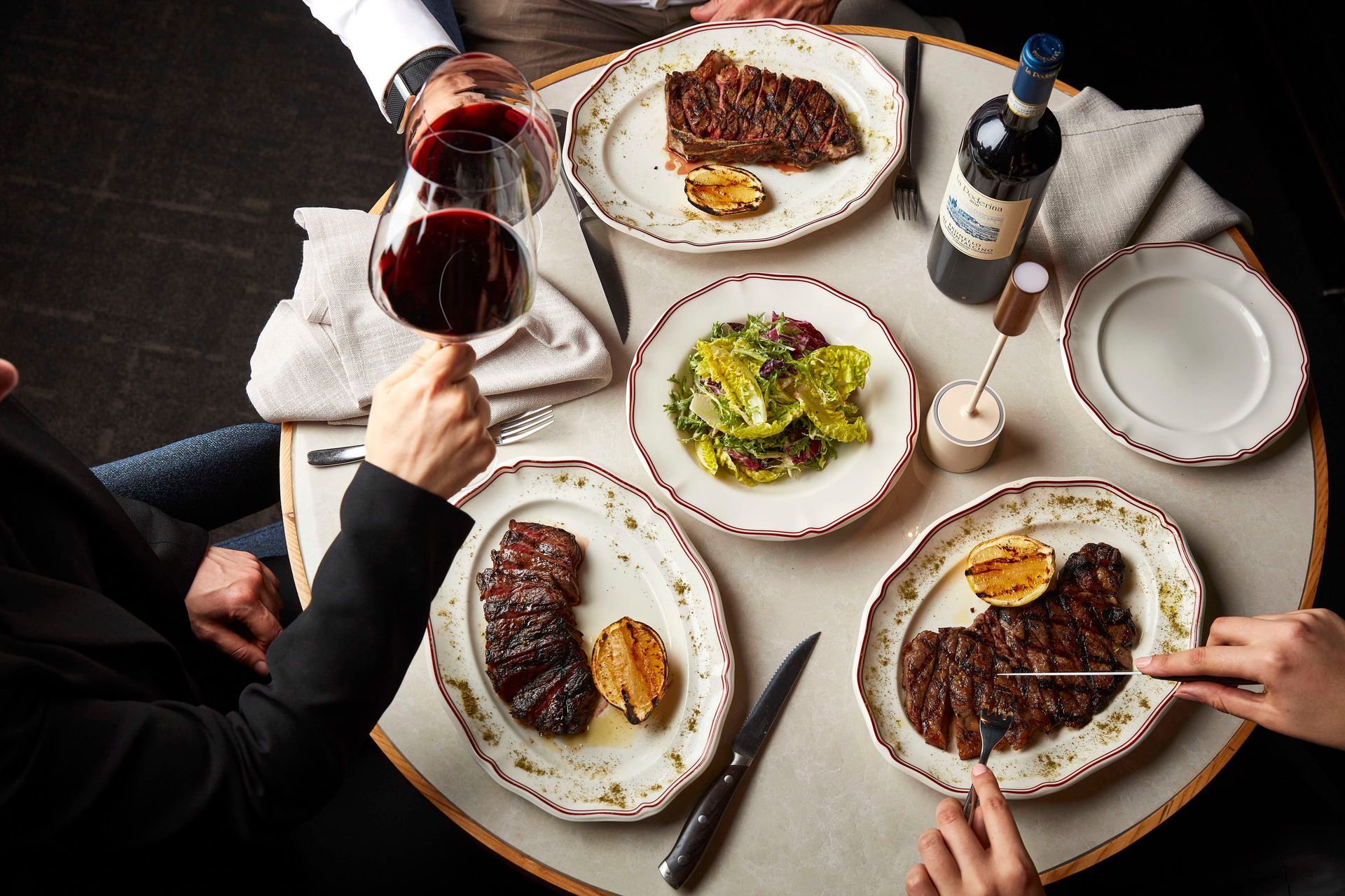 Restaurant table set for a meal, with wine glasses and a plated dish in front of a city view.